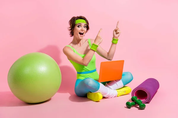 Photo of amazed sporty lady coach using netbook pointing empty space sport club promo isolated over pastel color background.