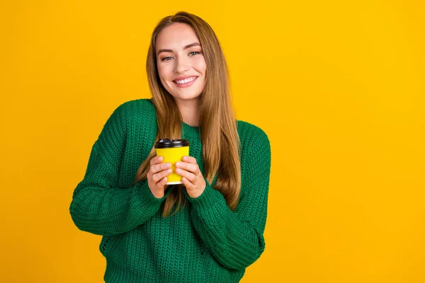 Photo of young cute woman wear green jumper holding warm beverage in office during coffee break isolated on yellow color background.