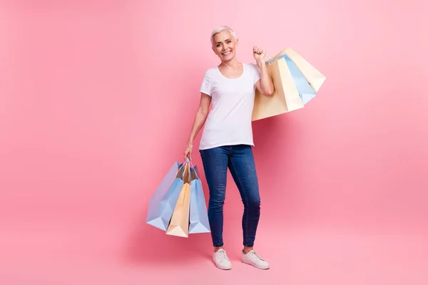 陽気な女性のフルサイズの写真は ピンク色の背景に隔離された黒の金曜日にショッピングバッグを保持する白いTシャツジーンズを着用します — ストック写真