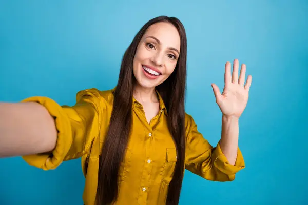 Photo of adorable excited lady wear yellow shirt recording video vlog waving arm hi isolated blue color background.