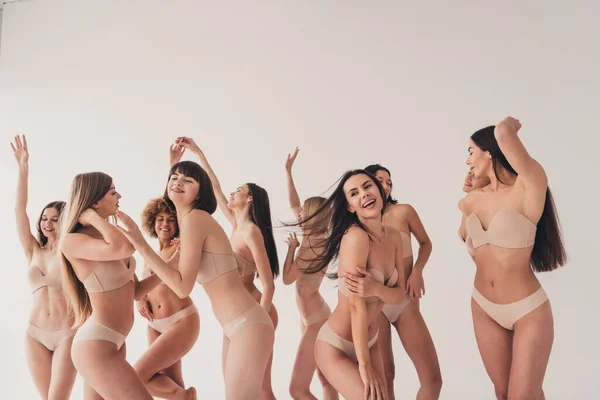 Studio no retouch photo of carefree shiny ladies dressed lingerie having fun enjoying all beautiful bodies isolated beige color wall background.