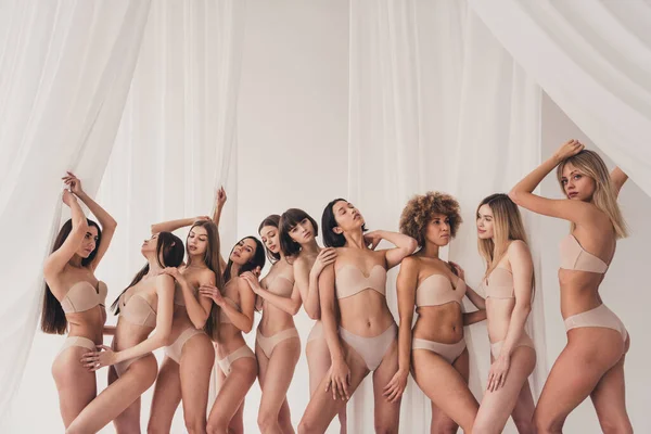 No filter photo of friends group of women with different body types in underwear posing together on light background.