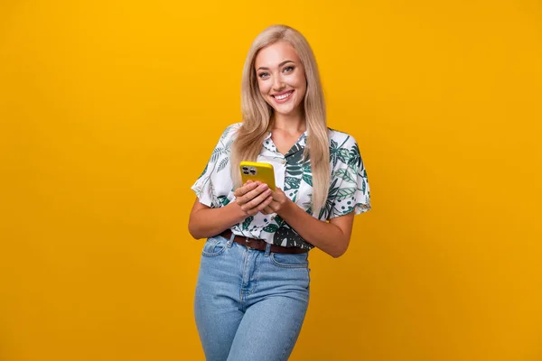 Photo of intelligent pretty woman with straight hairdo dressed print shirt hold smartphone smiling isolated on yellow color background.
