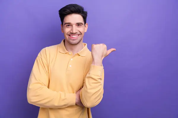 良い気分の写真 魅力的な男は親指の空白スペースを指す黄色いシャツを着て 紫色の背景を隔離しました — ストック写真