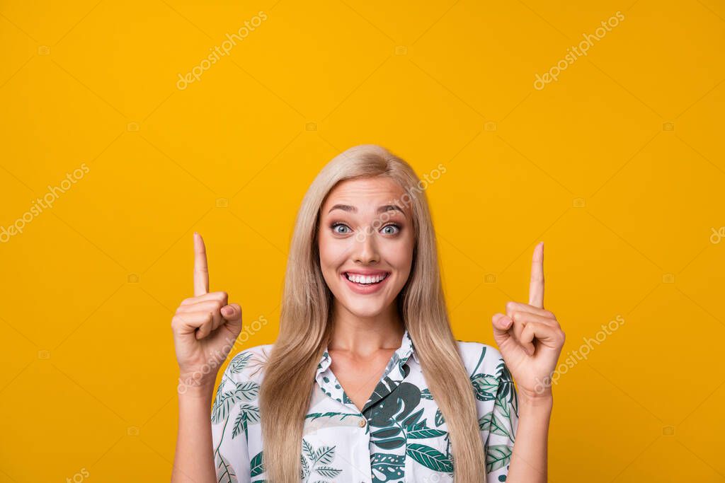Photo of funny positive woman with straight hair dressed print shirt directing at promo empty space isolated on yellow color background.