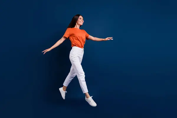 全长照片 穿着橙色T恤的漂亮女人跳过高空荡荡的空间 孤立的深蓝色背景 — 图库照片