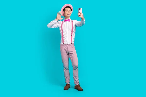 Full length photo of cheerful man dressed pink retro cap pants waving palm on smartphone doing selfie isolated on blue color background.