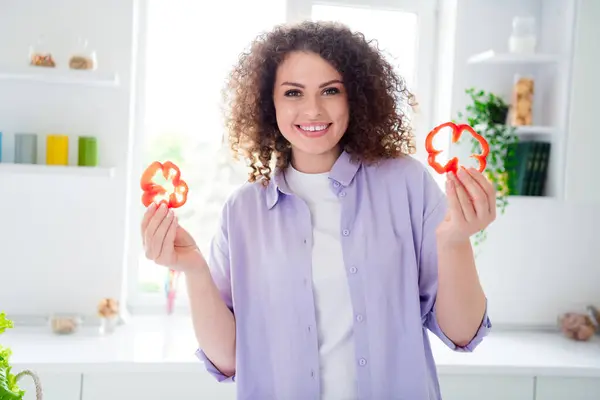 Photo of excited charming lady dressed purple shirt cooking breakfast rising fresh sweet red pepper slices indoors house kitchen.