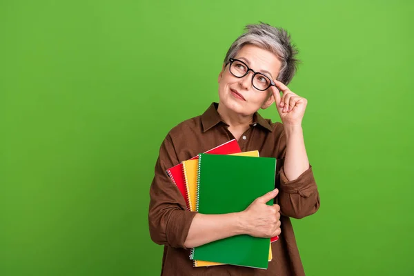Portrait of minded person with white gray hairstyle touch glasses hold notebooks look empty space isolated on green color background.