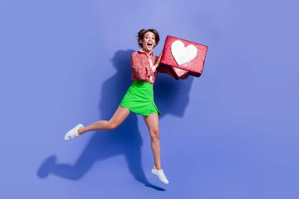 Full length photo of charming ecstatic girl wear green skirt jumping with social media like in hands isolated on blue color background.