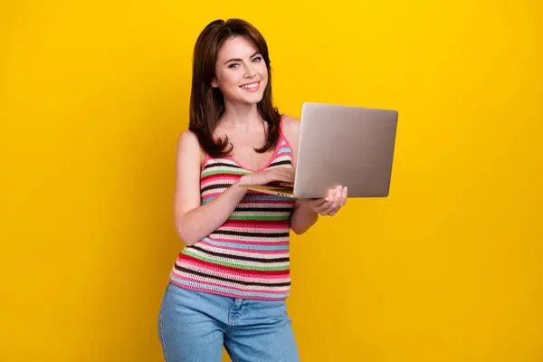 Photo of intelligent lovely cute girl with stylish hairdo wear striped tank holding laptop in hand isolated on yellow color background.