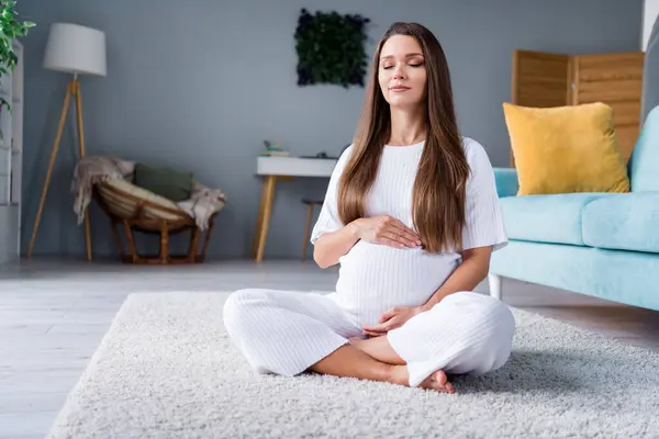 Photo of calm peaceful cute adorable mom pregnant girl sitting on fluffy carpet practicing yoga spiritual practice.