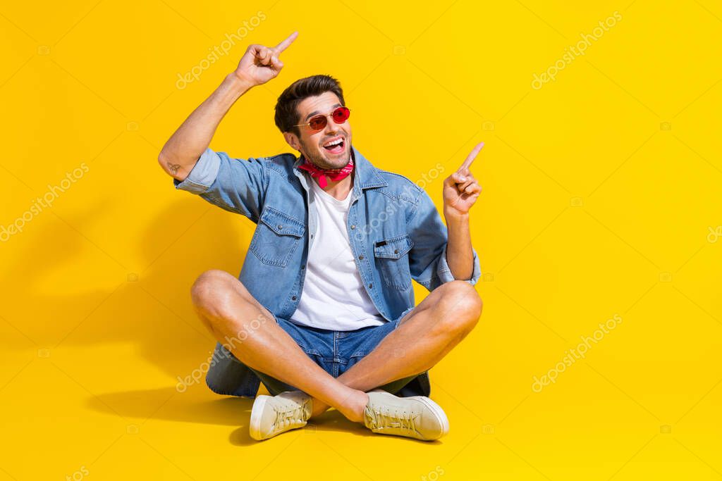 Full body photo of impressed man dressed denim shirt shorts sit directing look at sale empty space isolated on yellow color background.