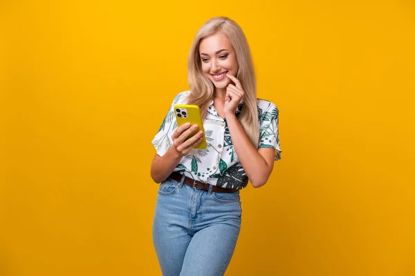 Photo of minded clever woman with straight hairdo dressed print shirt look at smartphone read sms isolated on yellow color background.