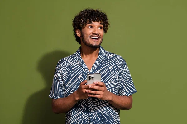 Photo of positive excited guy wear print shirt chatting modern device looking empty space isolated khaki color background.