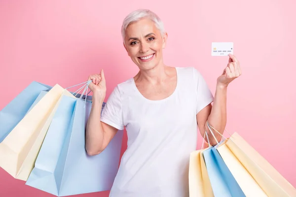 スタイリッシュなTシャツを着た陽気な人の肖像画 ショッピングバッグ ピンクの背景に隔離されたクレジットカードのワイヤレス決済を実証します — ストック写真