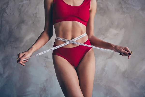 No retouch photo of body positive slim woman dressed red underwear keep measuring tape on waist isolated on gray concrete background.