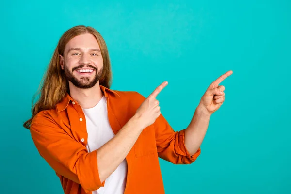 Photo of young guy with mustache and long blond hair pointing fingers empty space advertising barbershop isolated on cyan color background.