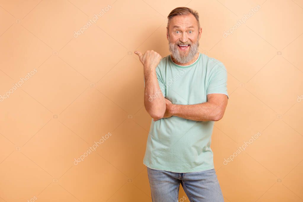 Photo of overjoyed man with white beard dressed teal t-shirt indicating at awesome sale empty space isolated on beige color background.