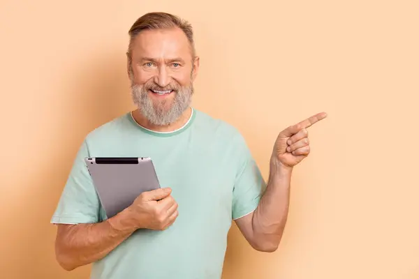 照片上 友善的老年人穿着单调的T恤衫 手持平板电脑 上面标明空旷的空间 与米色背景隔离 — 图库照片