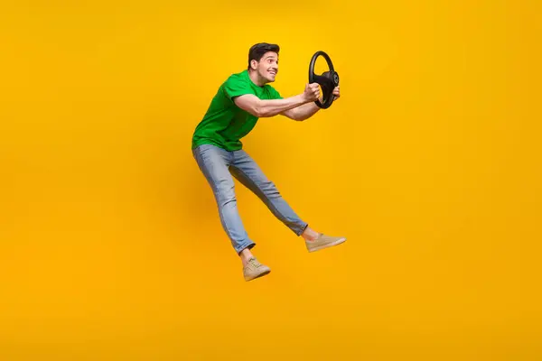 stock image Full size photo of excited guy wear stylish t-shirt jumping hold steering wheel ride invisible vehicle isolated on yellow color background.