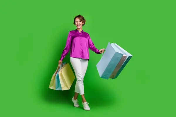 緑色の背景に隔離された袋を運ぶマゼンタの服を着たポジティブかわいい女の子の完全な長さの写真 — ストック写真