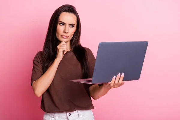 Photo of young funny business woman touch chin when brainstorm ponder look at laptop serious expression isolated on pink color background.