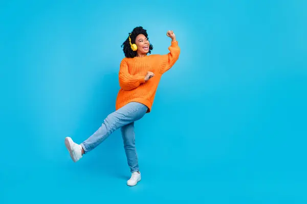 迷人的年轻女子跳舞耳机的全貌照片 音乐穿着时髦的针织橙色衣服 背景是蓝色的 — 图库照片