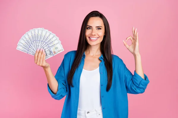 stock image Photo of toothy beaming girl with straight hairdo dressed blue shirt hold money showing okey good job isolated on pink color background.