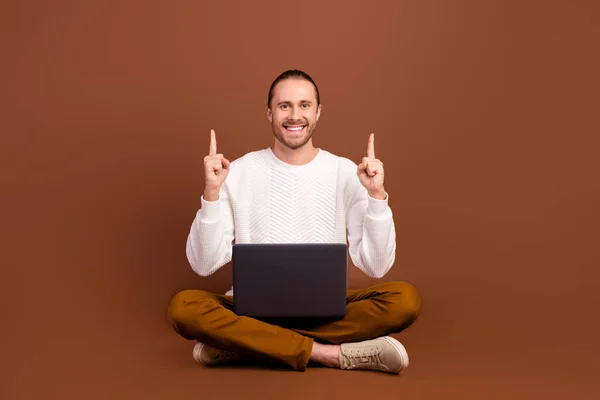 Full length photo of cool cheerful guy dressed white pullover working modern gadget two finger empty space isolated brown color background.