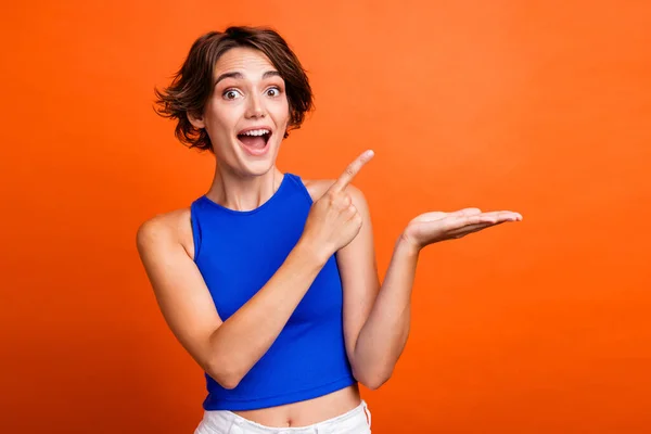 Photo of excited funky lady wear blue singlet showing finger arm empty space isolated orange color background.