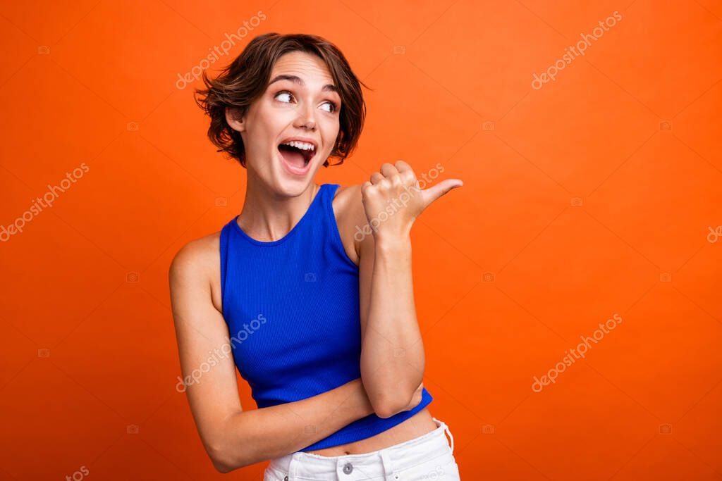 Photo of pretty excited lady wear blue singlet pointing thumb looking empty space isolated orange color background.