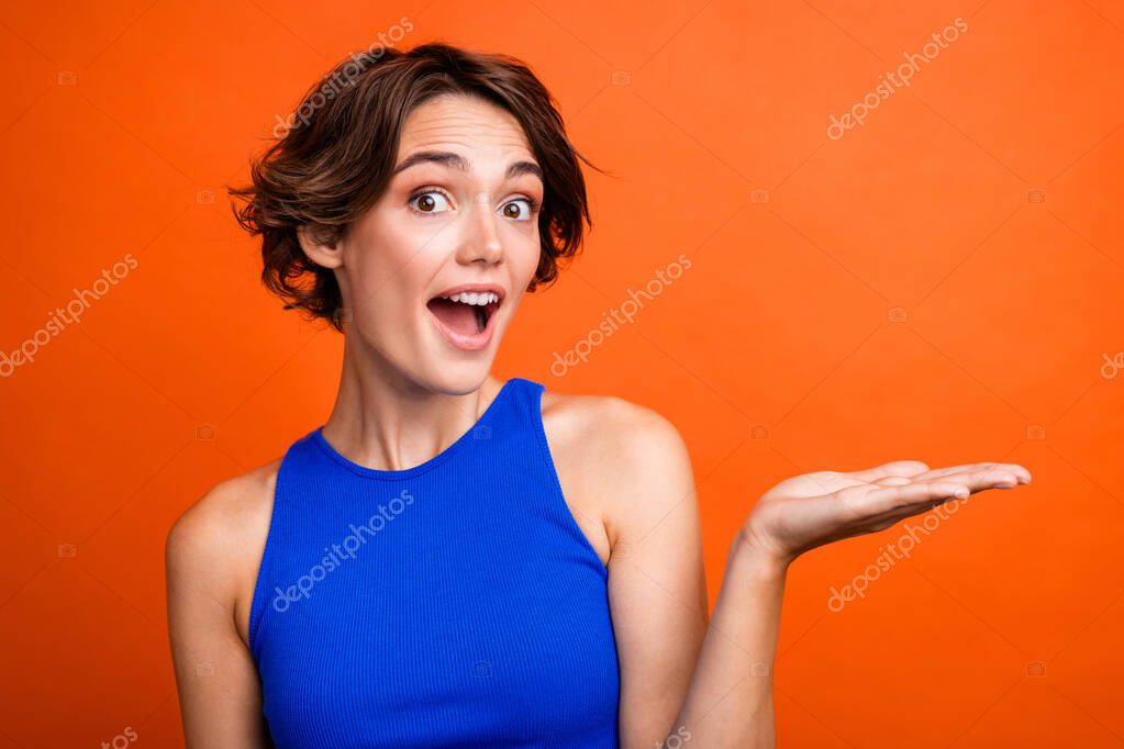 Photo of impressed funky girl dressed blue top open mouth showing arm empty space isolated orange color background.