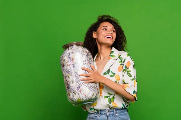 Photo of dreamy excited woman dressed print shirt looking empty space saving money glass jar isolated green color background.