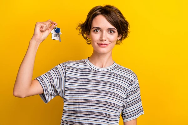 Photo of lovely cute girl dressed trendy clothes showing keys new flat isolated on yellow color background.