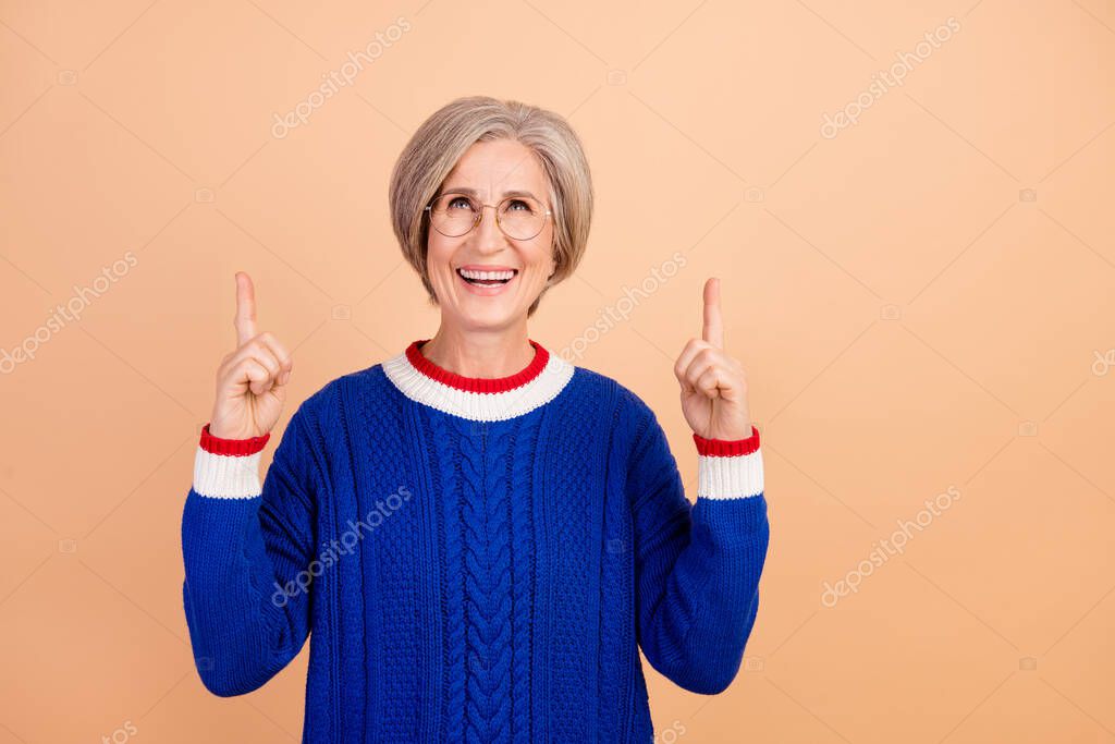 Photo of positive woman with gray hair dressed knit sweater look directing up at empty space logo isolated on beige color background.