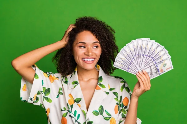 Photo of cheerful excited woman dressed print shirt arm head looking dollars fan isolated green color background.