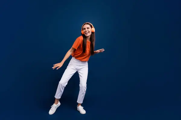 全长照片 可爱的甜女士戴着橙色T恤衫耳机跳舞迪斯科舞厅空旷的空间孤立的深蓝色背景 — 图库照片