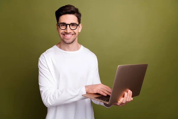 Photo of young optimistic system administrator man in white pullover typing keyboard his netbook isolated on khaki color background.