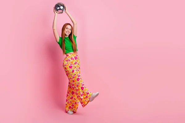 ポジティブな陽気な少女のフルサイズの写真は ピンク色の背景に隔離された頭の上にディスコボールを保持スタイリッシュなトッププリントパンツを着用します — ストック写真