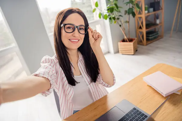 迷人而快乐的女士坐在椅子扶手触摸眼镜的照片 让自己成为写字台笔记本电脑在室内的商务中心 — 图库照片