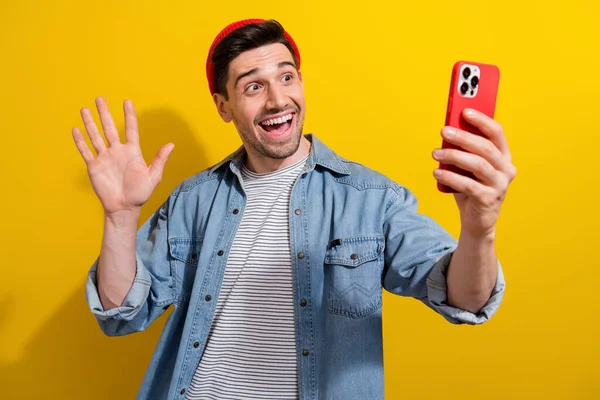 Photo of cool excited man dressed jeans shirt waving arm hi recording video vlog modern gadget isolated yellow color background.