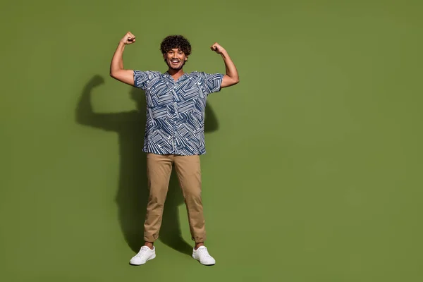 Full body size photo of young sportsman standing raised fists up showing his fit big biceps muscles isolated over khaki color background.
