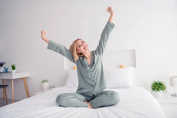 Full length body photo of young blonde girl in cozy grey victoria secret brand pajama wake up morning raised fists yawning indoors.