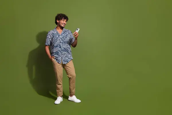 Full length photo of cool funky man dressed print shirt chatting modern gadget empty space isolated green color background.
