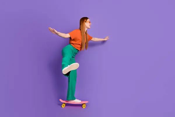Photo of lovely pretty good mood girl dressed stylish clothes riding long board empty space isolated on purple color background.