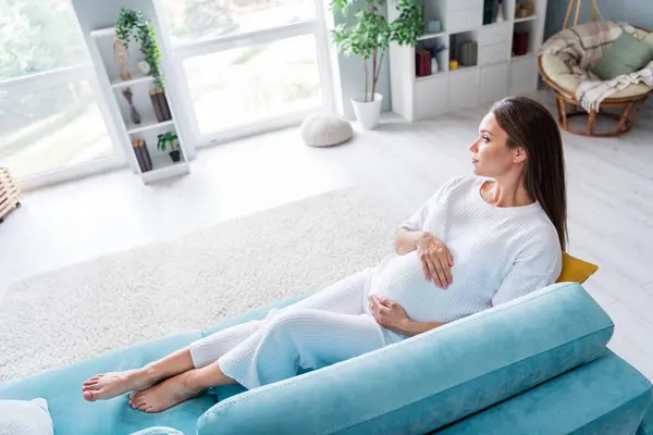 Photo of lovely pretty adorable pregnant girl future mum sitting soft divan waiting for childbirth modern flat living room interior.