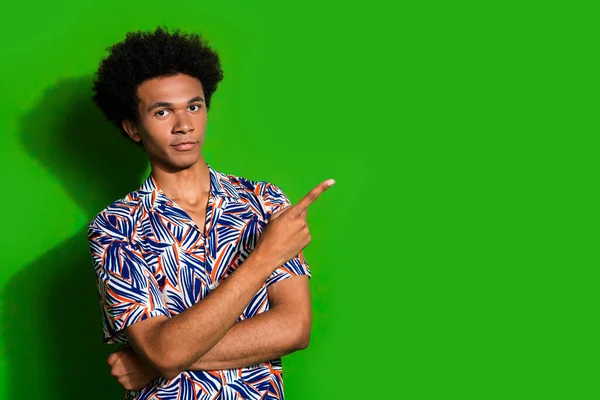Photo of youngster guy student in trend print shirt point finger empty space recommend exotic shop isolated on green color background.