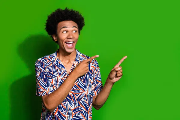 Portrait of funny guy wearing print shirt and astonished pointing fingers empty space introduce ads isolated on green color background.