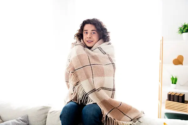 Photo of cheerful funky guy rolling plaid blanket freezing feeling cold indoors room home house.